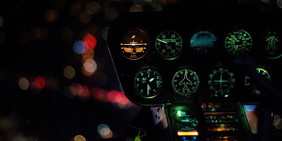 Illuminated cockpit gauges of a helicopter flying at night over city lights.