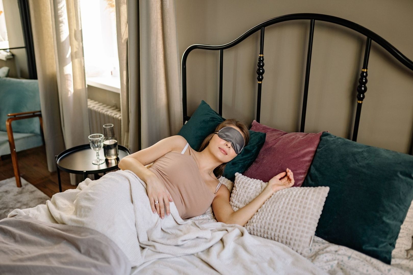 Woman wearing an eye mask rests under blankets in bed