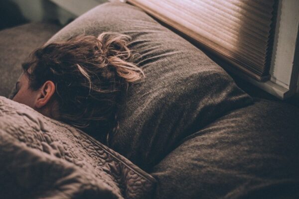 Person sleeping under blankets beside a window, illustrating deep rest