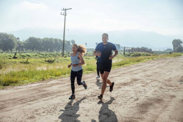 Two runners jog together on a sunlit rural dirt road