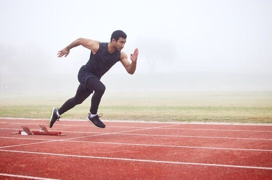 Runner accelerating from starting blocks on a red track